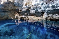 blue water in a cave with a rope attached to it