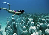 a woman snorks in front of a group of statues