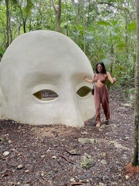 a woman standing next to a large white sculpture in the woods